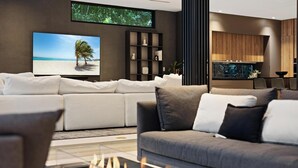 A modern living room with a fireplace, a large flat-screen TV, a bookshelf, and a kitchen area with wooden cabinets. - Villa Strata: Modern 5 BED +POOL, minutes from The Grove, Brickell & Downtown (Miami)