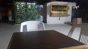 A dining area with a wooden table and white chairs, a wall-mounted light fixture, and a green leafy plant. - Hostal Casa Gavilan (Tecamac)