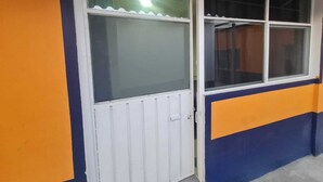 A room with a white door and two windows, one with a curtain and one without. - Hostal Casa Gavilan (Tecamac)