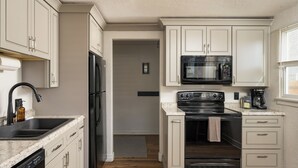 Eine Küche mit weißen Schränken, einem schwarzen Kühlschrank, einer Mikrowelle, einem Backofen und einem Geschirrspüler.
