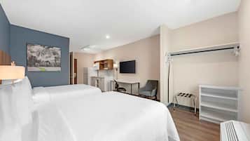 Een hotelkamer met twee bedden, een bureau, een stoel, een televisie, een kapstok en een plank.