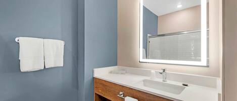 A modern bathroom with a large mirror, white sink, and wooden vanity.