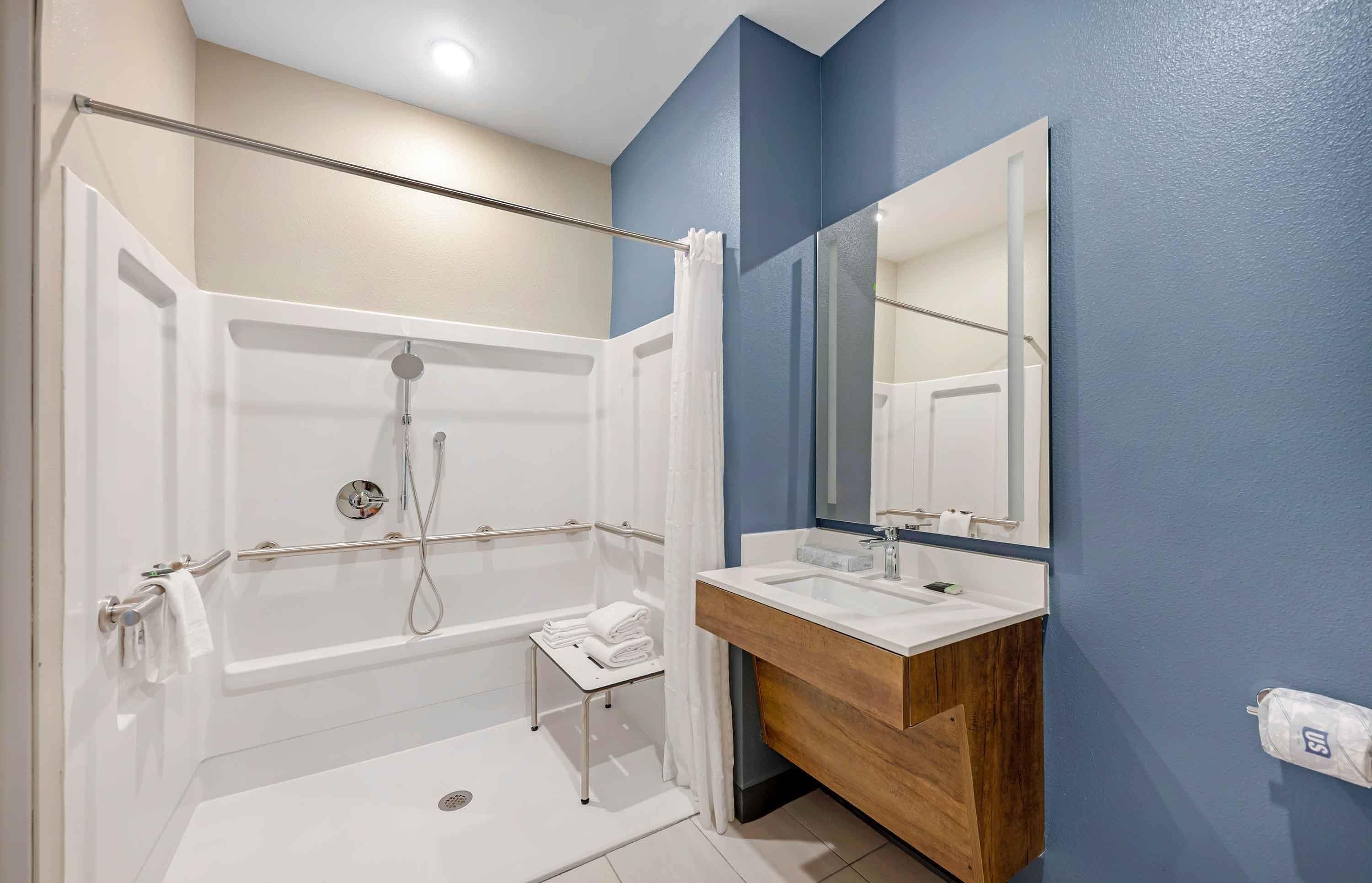 A modern bathroom with a walk-in shower, a vanity with a mirror, and a towel rack.