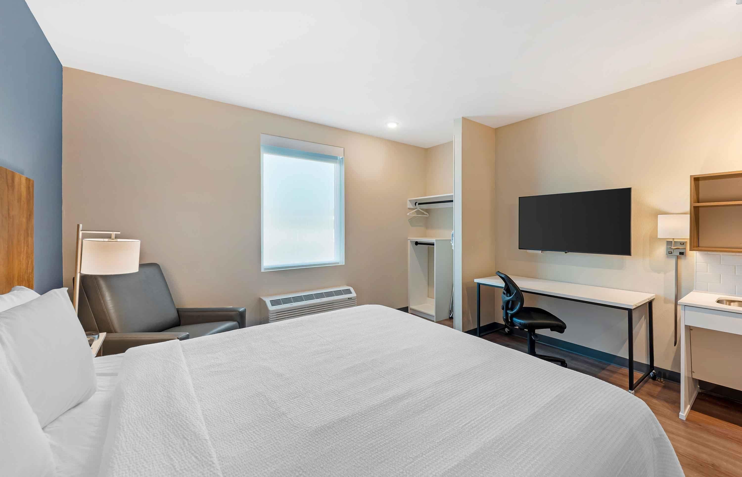 Habitación de hotel con cama, escritorio, silla, televisor y ventana.