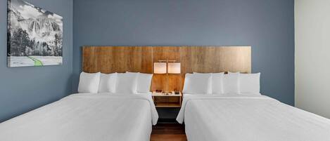 Une chambre d’hôtel avec deux lits, une tête de lit en bois, une table de chevet avec une lampe et un tableau encadré au mur.