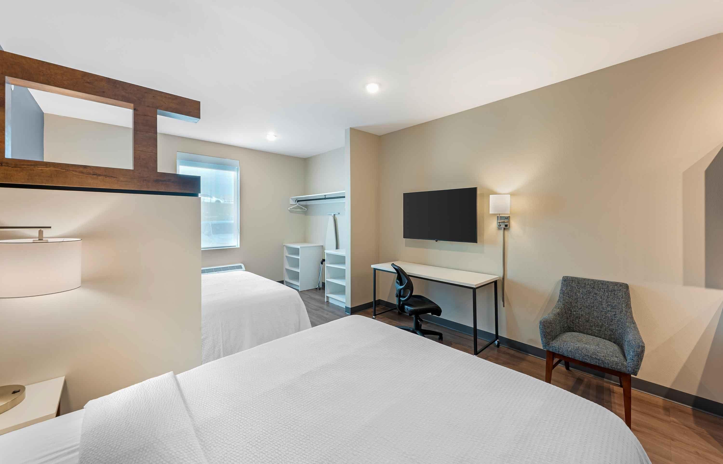 A hotel room with two beds, a desk, a chair, a TV, and a mirror.