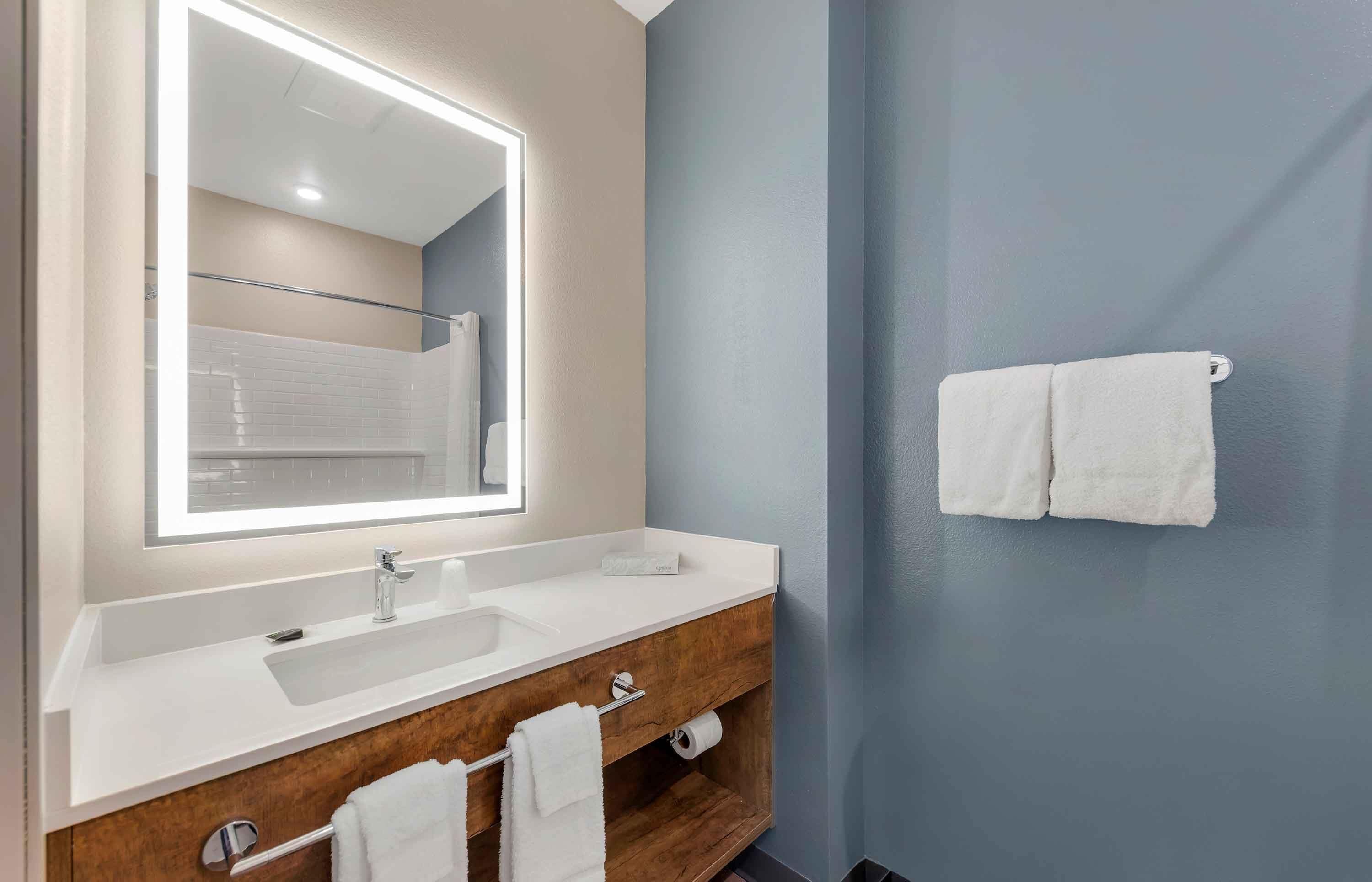 A modern bathroom with a large mirror, white sink, and wooden vanity.