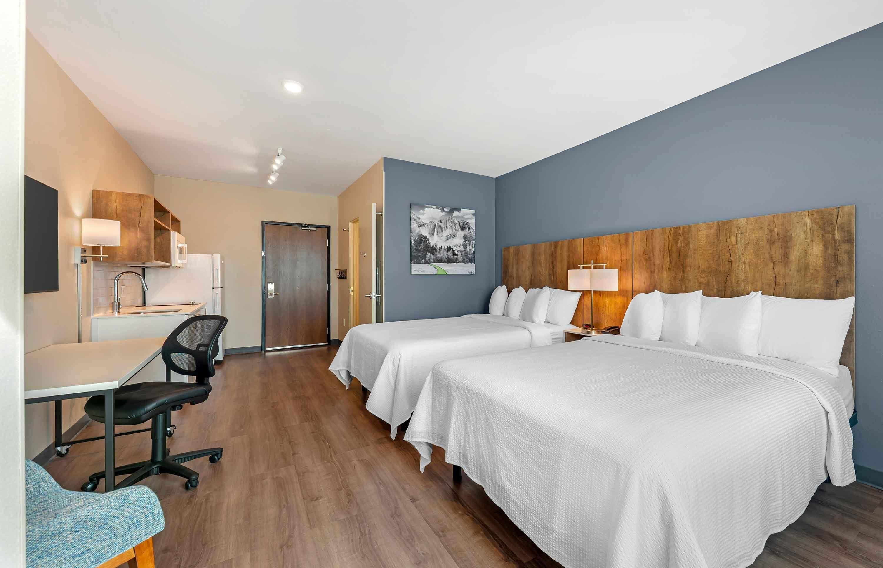 A hotel room with two beds, a desk, a chair, and a large wooden headboard.