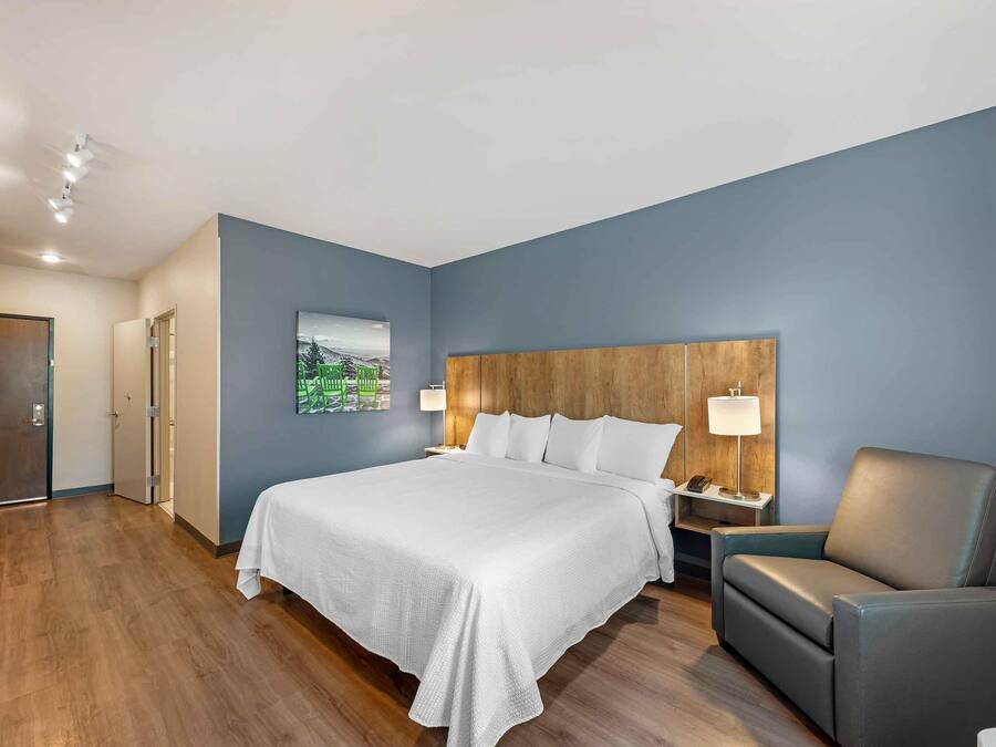 A hotel room with a large bed, a wooden headboard, a nightstand, a desk, and a chair.