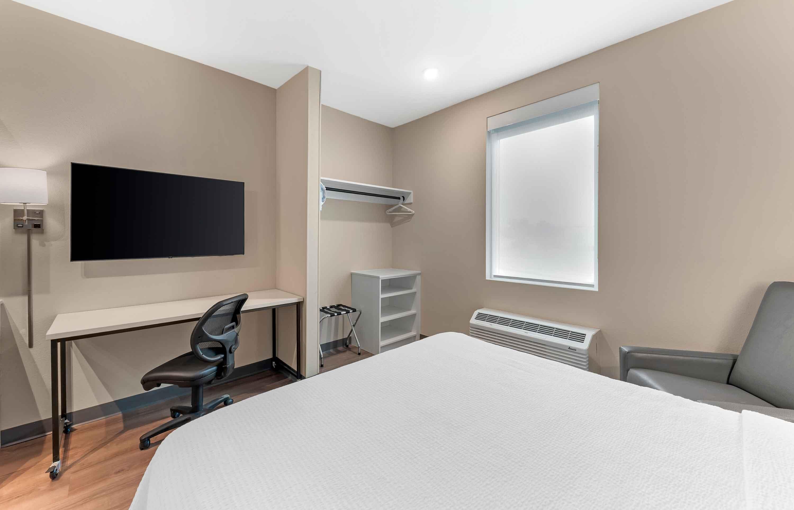 A hotel room with a bed, desk, chair, TV, wardrobe, and a window.