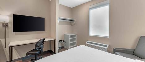 Habitación de hotel con cama, escritorio, silla, televisor, armario y ventana.