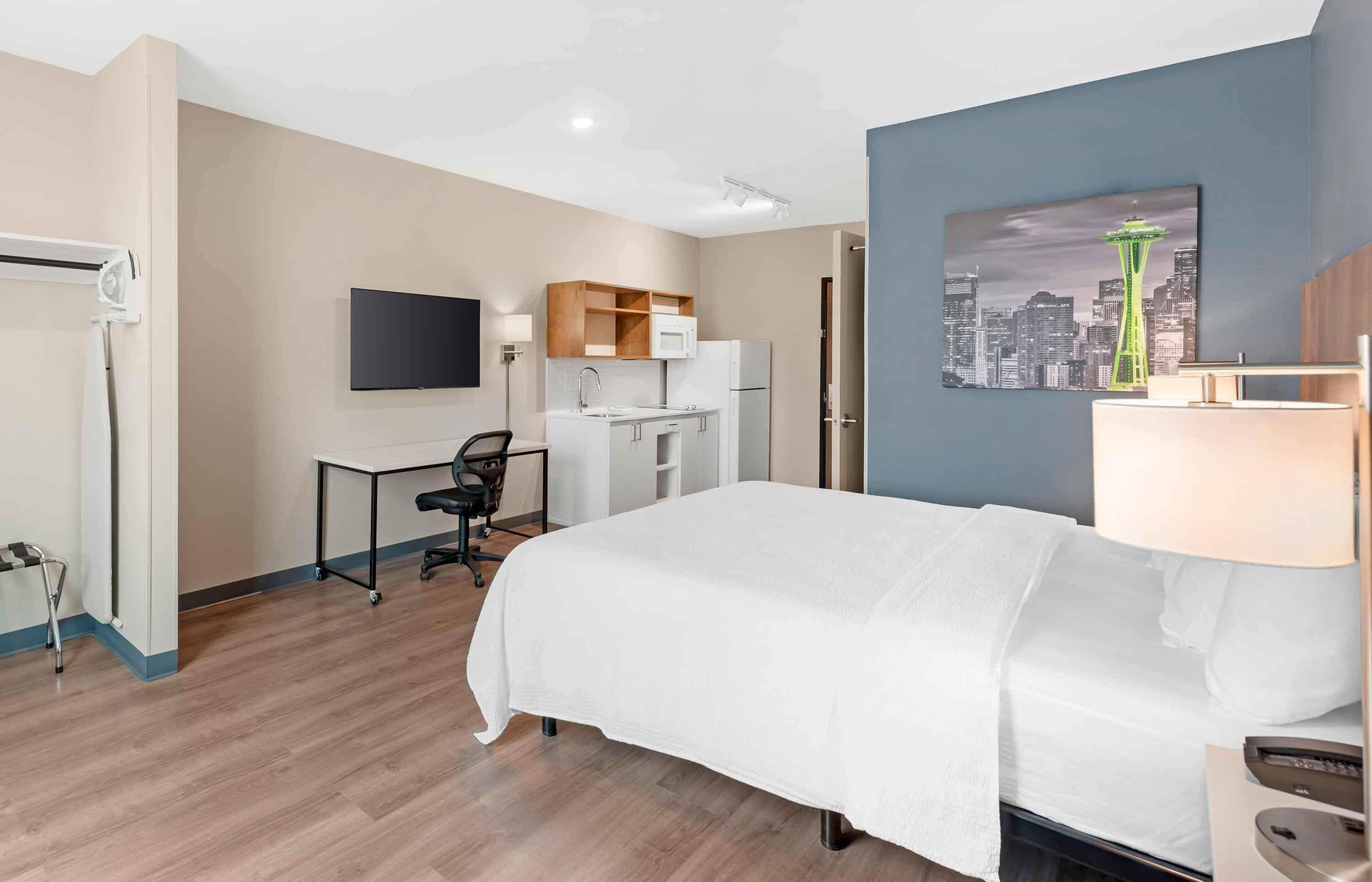 A hotel room with a bed, desk, chair, and a cityscape painting on the wall.