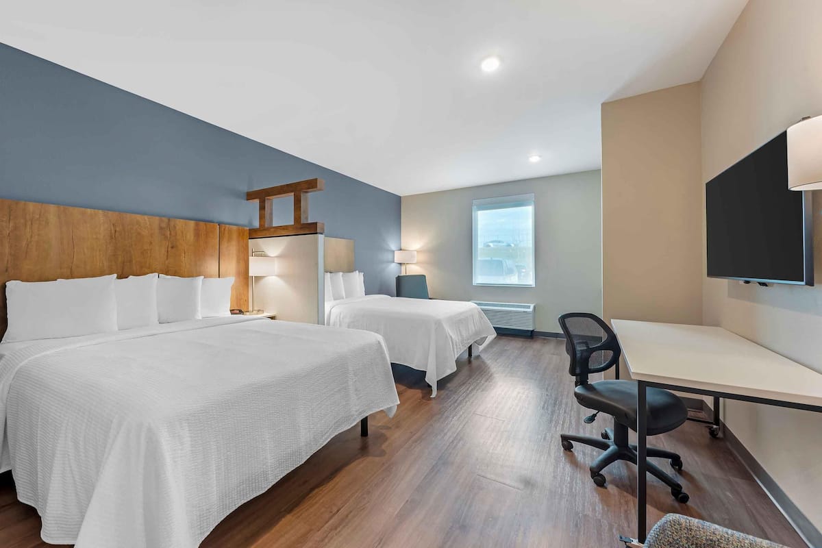 A hotel room with two beds, a desk, a chair, a TV, and a window with a view.