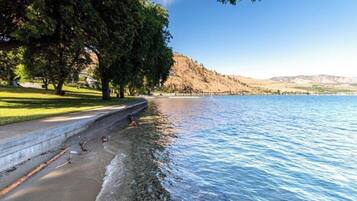 Un parque junto al lago con un sendero, árboles y vistas a las colinas en la distancia.