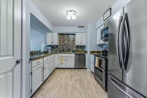 Une cuisine moderne avec des armoires blanches, des appareils en acier inoxydable et un pare-feu décoratif.