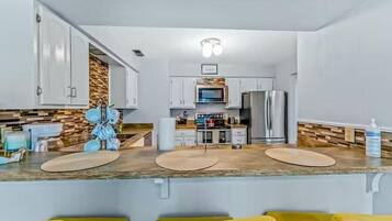 Una cocina moderna con armarios blancos, microondas y refrigerador. Hay dos sillas amarillas al frente.