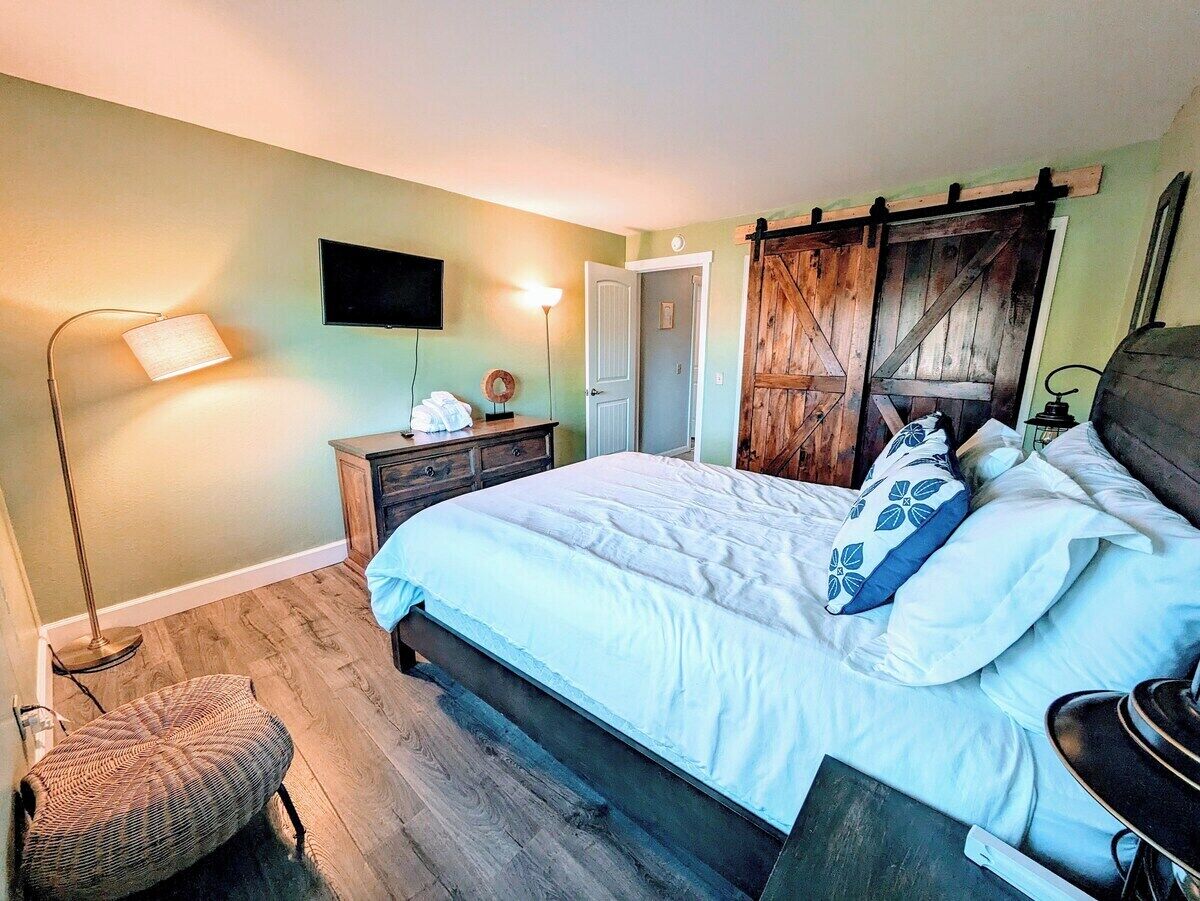 A bedroom with a bed, bedside tables, a lamp, a TV, and a door.