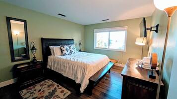 Un dormitorio con cama, mesitas de noche, un espejo, una ventana y suelo de madera.