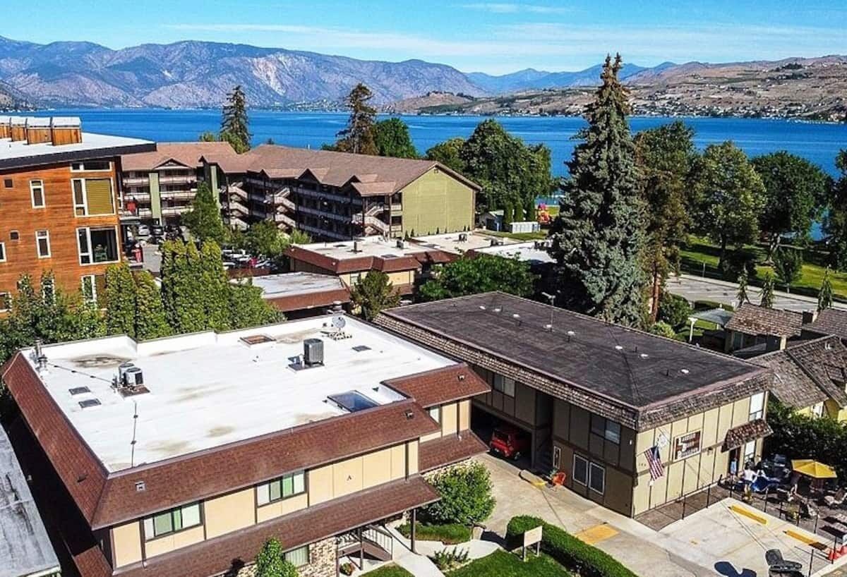 A multi-story building with a flat roof, a parking area, and a view of a lake and mountains in the background.