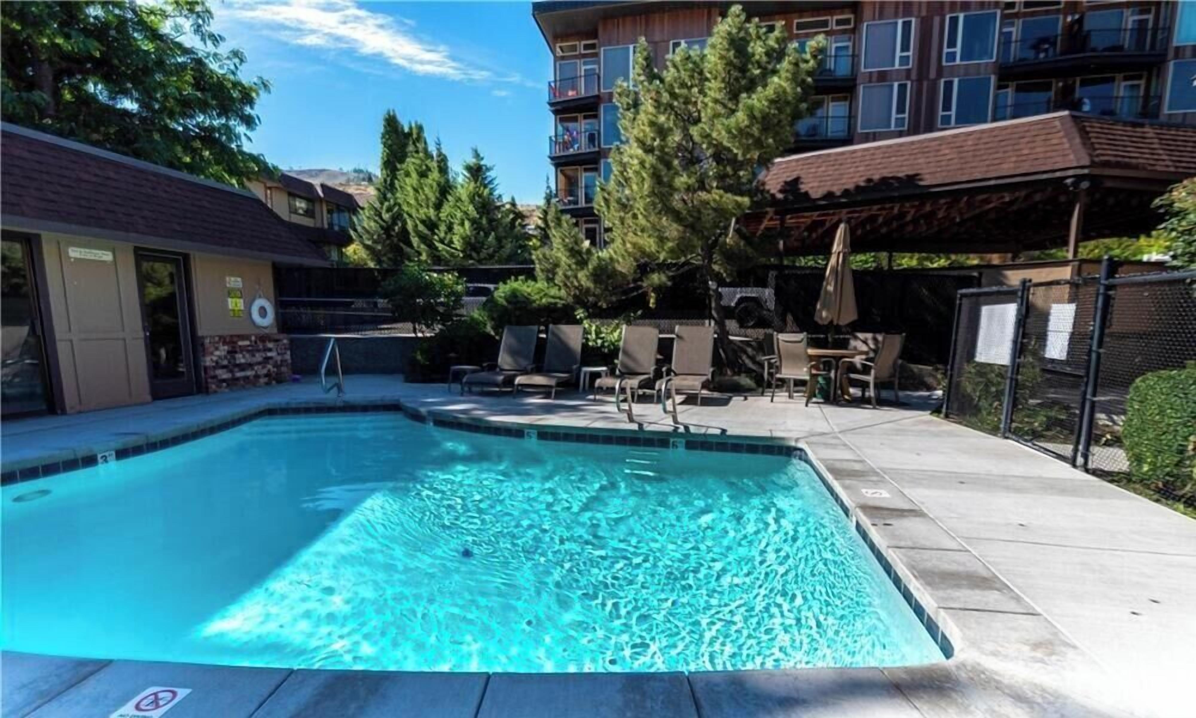A swimming pool with a lounge area, surrounded by buildings and trees.