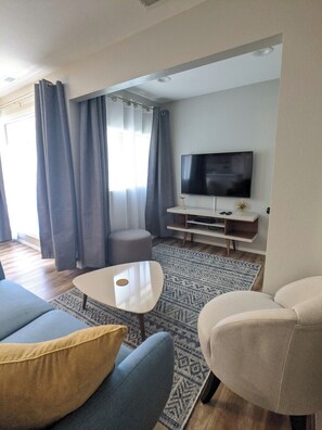 Ein modernes Wohnzimmer mit Flachbildfernseher, Couchtisch und Sitzgelegenheiten.