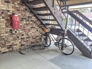 Una bicicleta sujeta a un soporte, un extintor de incendios fijado a una pared de ladrillo y una escalera con barandillas metálicas.