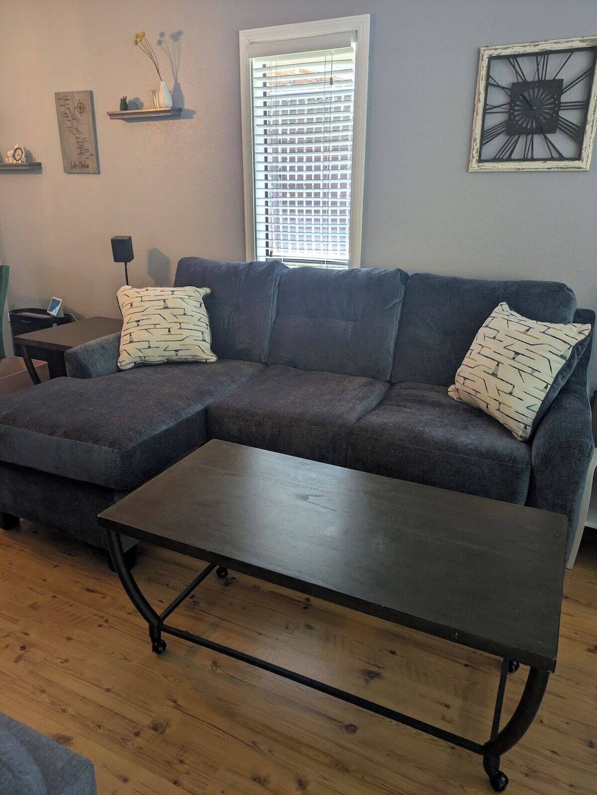 A living room with a sectional sofa, a coffee table, a side table, a lamp, and a window with blinds.