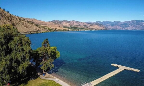 A lake with a dock extending into the water, surrounded by hills and trees. - Spacious Family Friendly Townhome at Lakeside Park (Chelan)