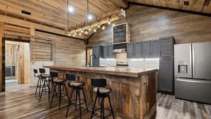 A modern kitchen with a wooden island, bar stools, stainless steel appliances, and a rustic ceiling. - Serenity found in this large, lodge-style 4-bedroom house surrounded by nature (Goreville)