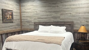 A bedroom with a wooden ceiling fan, a bed with white bedding, a wooden bench, and a small round table with a lamp. - Serenity found in this large, lodge-style 4-bedroom house surrounded by nature (Goreville)