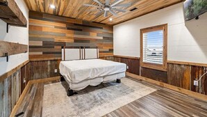 A bedroom with a wooden ceiling, a bed, a window, and a TV on the wall. - Serenity found in this large, lodge-style 4-bedroom house surrounded by nature (Goreville)