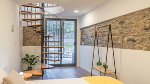 A modern bedroom with a spiral staircase, a bed with a yellow throw, a stone wall, and a hanging plant. - A View to Paradise – Spectacular Sea & Bay Views (Funchal)