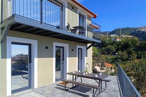 Un bâtiment moderne doté d’un balcon, d’une table avec des chaises et d’un fauteuil suspendu.