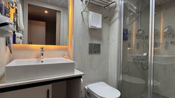 Un baño moderno con un espejo grande, un lavamanos blanco, un inodoro y una zona de ducha con mampara de vidrio.