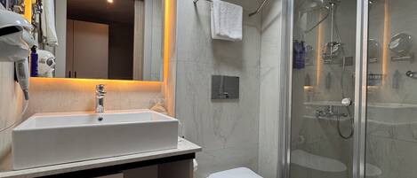 A modern bathroom with a large mirror, a white sink, a toilet, and a glass-enclosed shower area.
