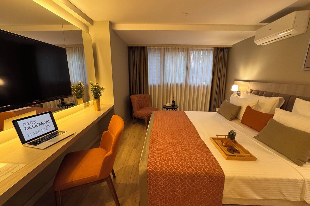 A hotel room with a bed, a desk with a laptop, a TV, and a chair.