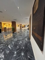 Un vestíbulo amplio con piso de mármol pulido, una zona de bar con taburetes y una obra de arte grande en la pared.