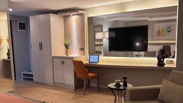 Une chambre d’hôtel moderne dotée d’un grand lit, d’un canapé, d’un bureau avec un ordinateur portable, d’une télévision et d’un coin cuisine.