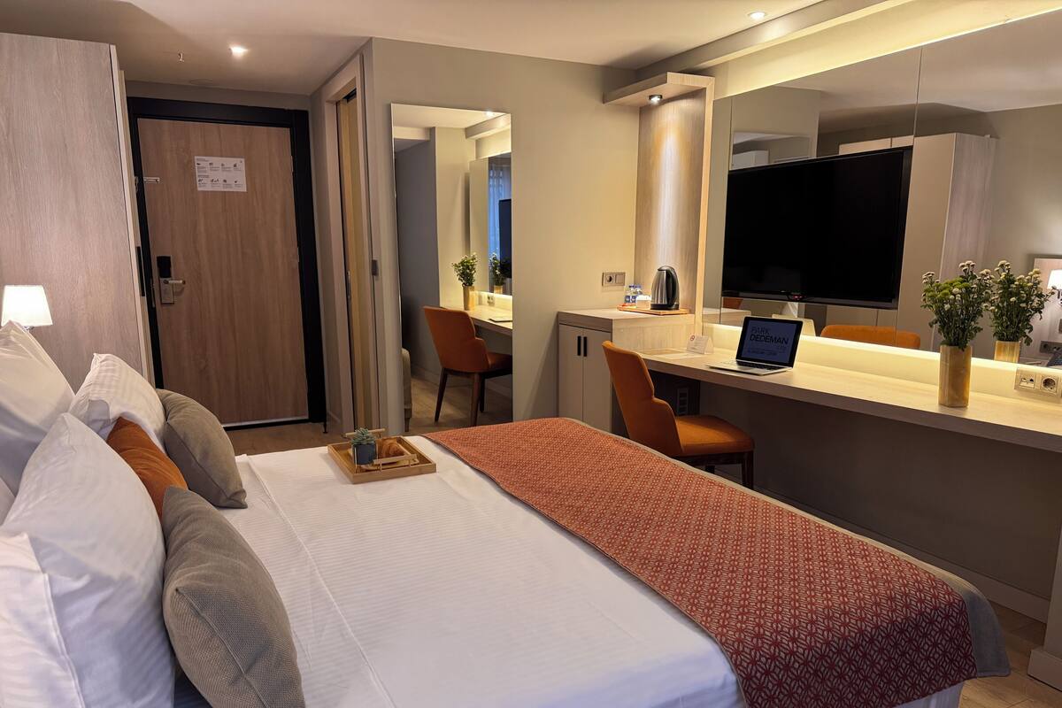 A hotel room with a bed, a desk, a chair, a television, and a mirror.