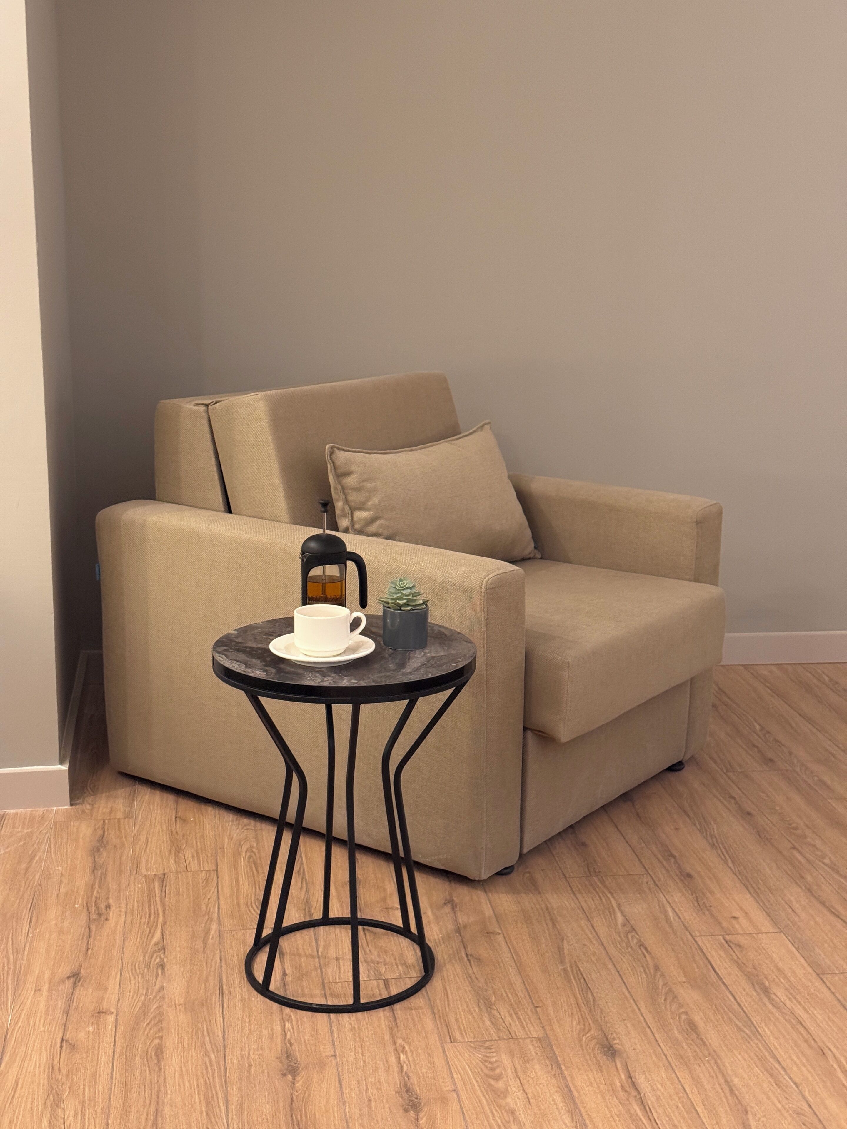A beige sofa with a small black table beside it, a white cup, and a small plant on the table.