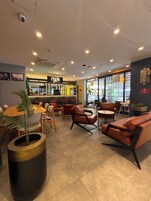 Un café moderno con barra, diferentes disposiciones de asientos y amplios ventanales que dejan entrar luz natural.