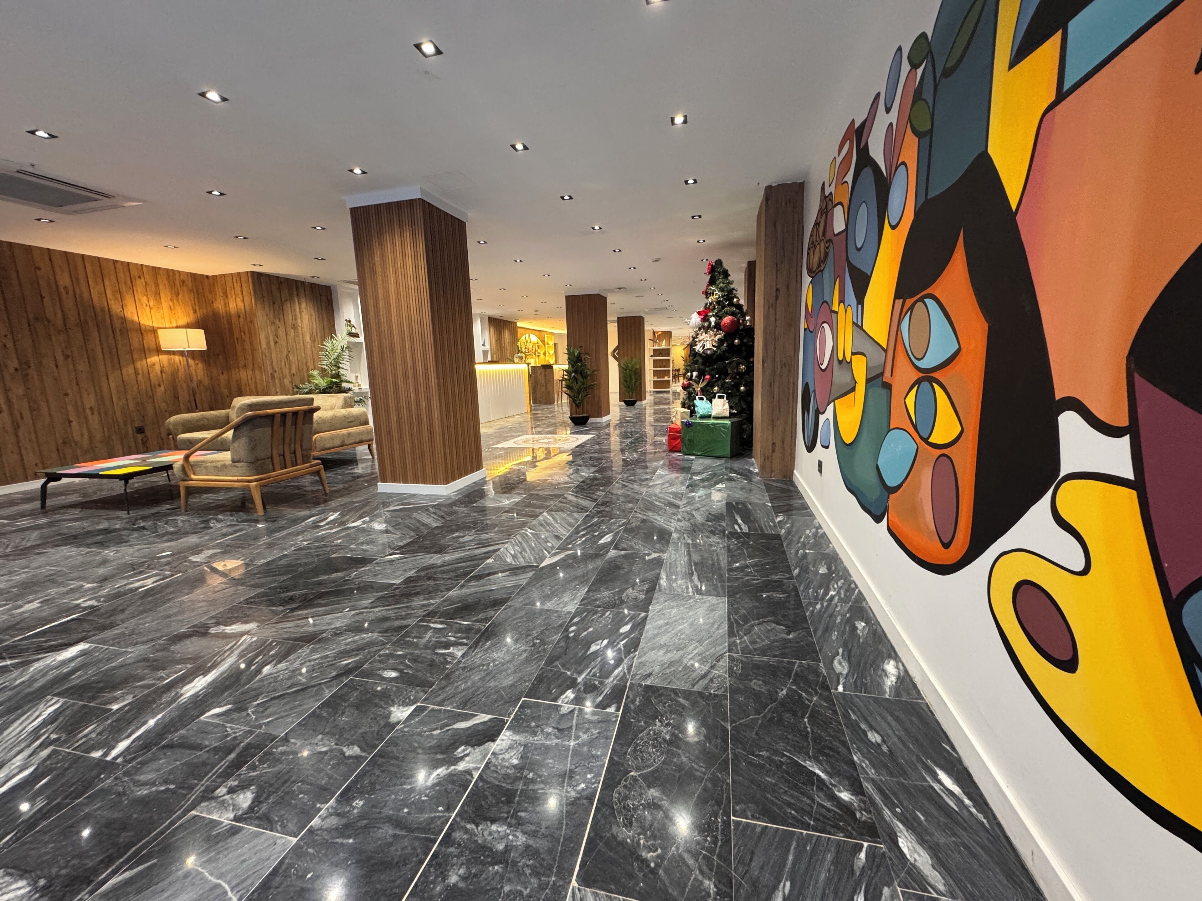 Un vestíbulo moderno con suelo de mármol, detalles de madera y un mural colorido.