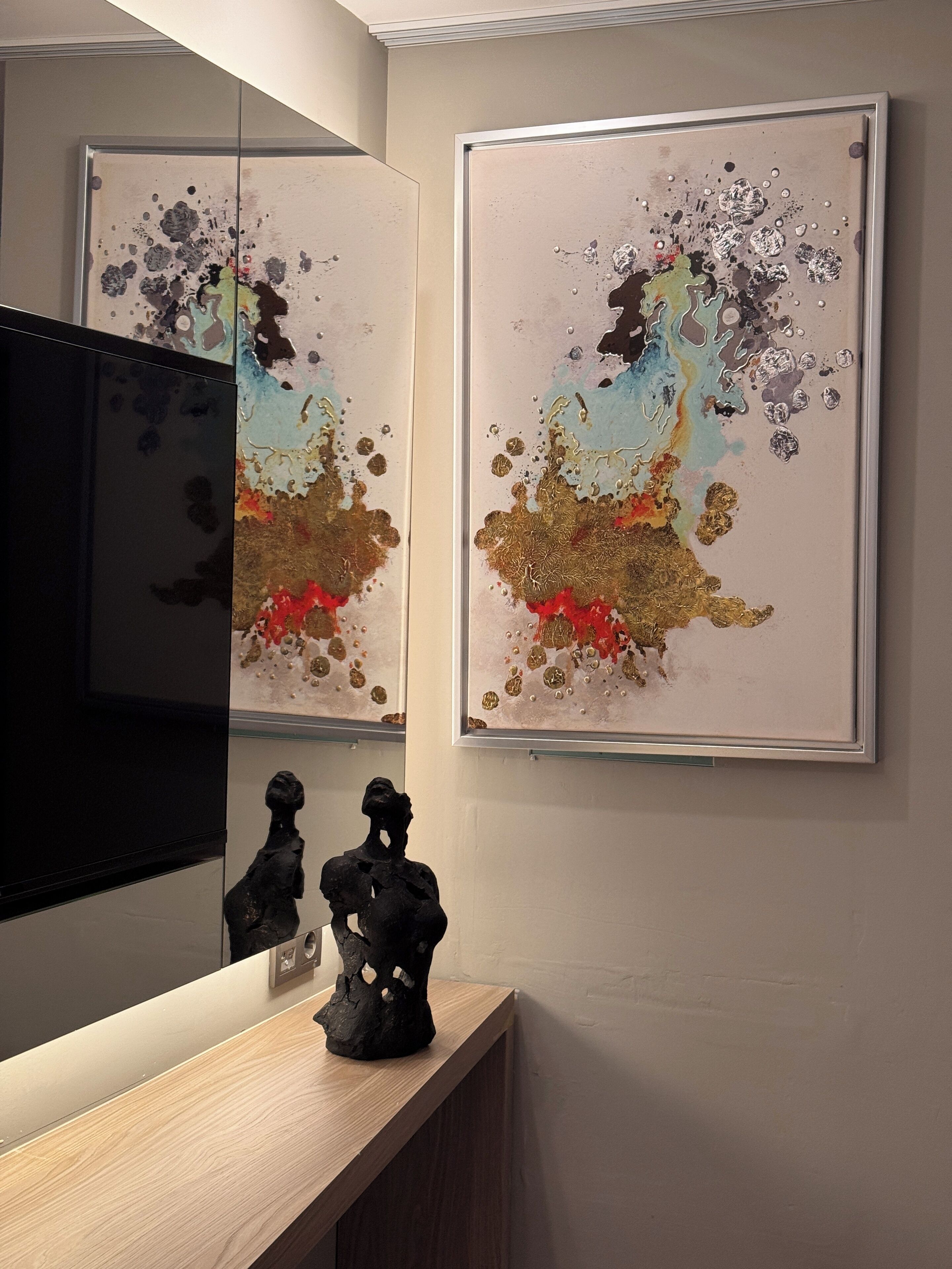 A modern interior with two abstract paintings on the wall, a wooden console table, and a sculpture.