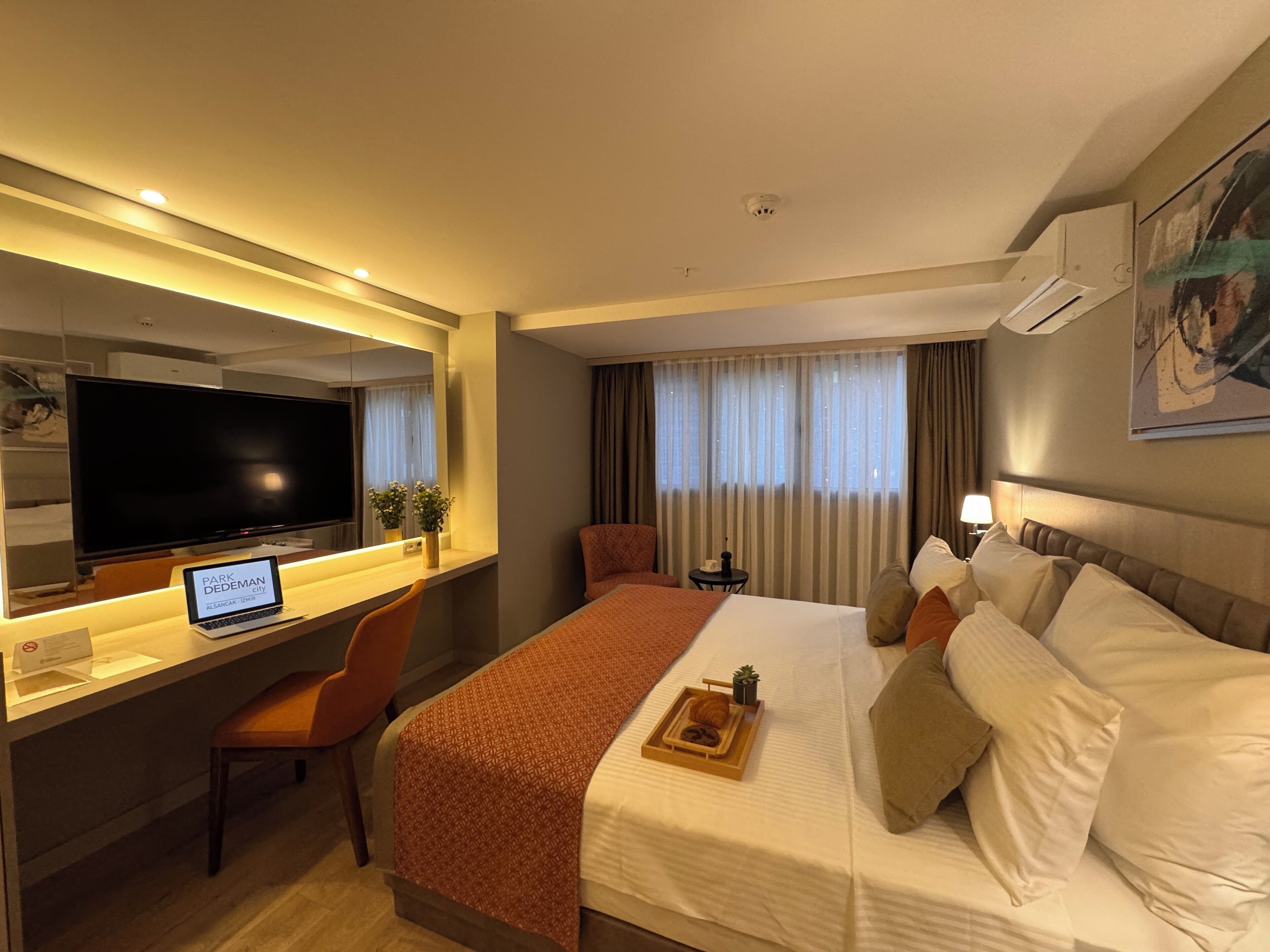 Una habitación de hotel con cama, escritorio con ordenador portátil, silla, televisión y ventana con cortinas.