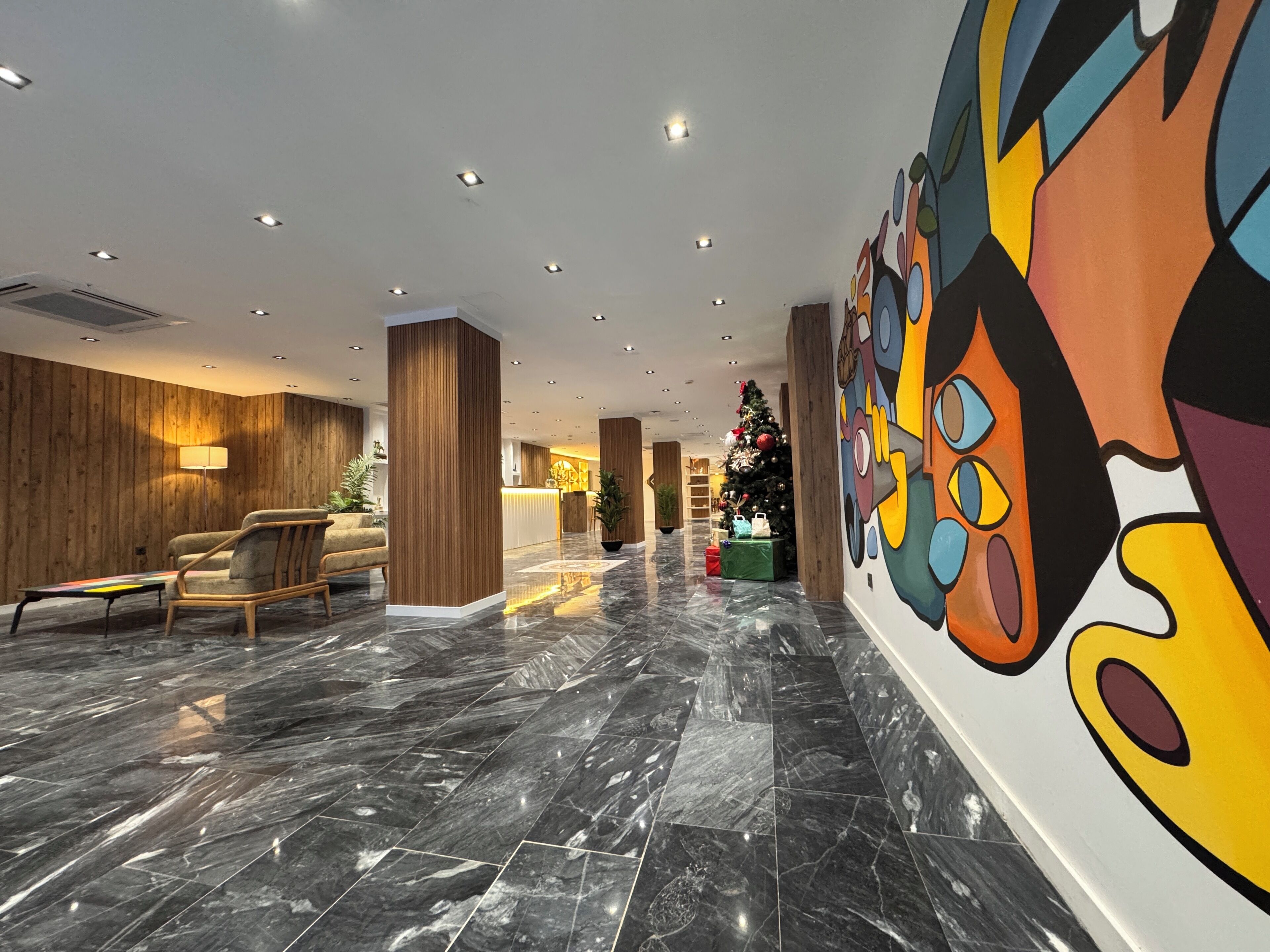 A modern lobby with a marble floor, wooden panel walls, and a colorful mural.