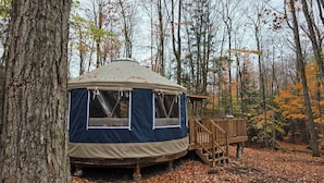 A circular yurt with a wooden deck, surrounded by trees with autumn leaves.