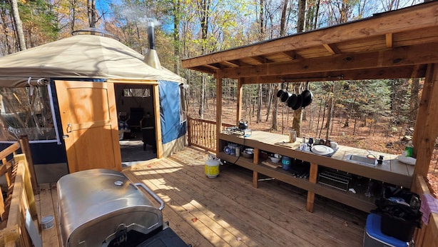 A wooden deck with a barbecue grill, a tent, and a covered dining area with hanging pots.