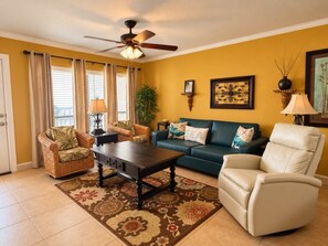 A living room with a sofa, armchairs, a coffee table, a ceiling fan, and a large window with curtains. - Saida III Condos - S3706 (South Padre Island)