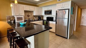 A modern kitchen with white cabinets, a large island, stainless steel appliances, and a tiled backsplash. - Saida III Condos - S3706 (South Padre Island)