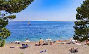 A beach with clear blue water, umbrellas, and people relaxing. - HOLIDAY HOME MONTEMARE (Tučepi)